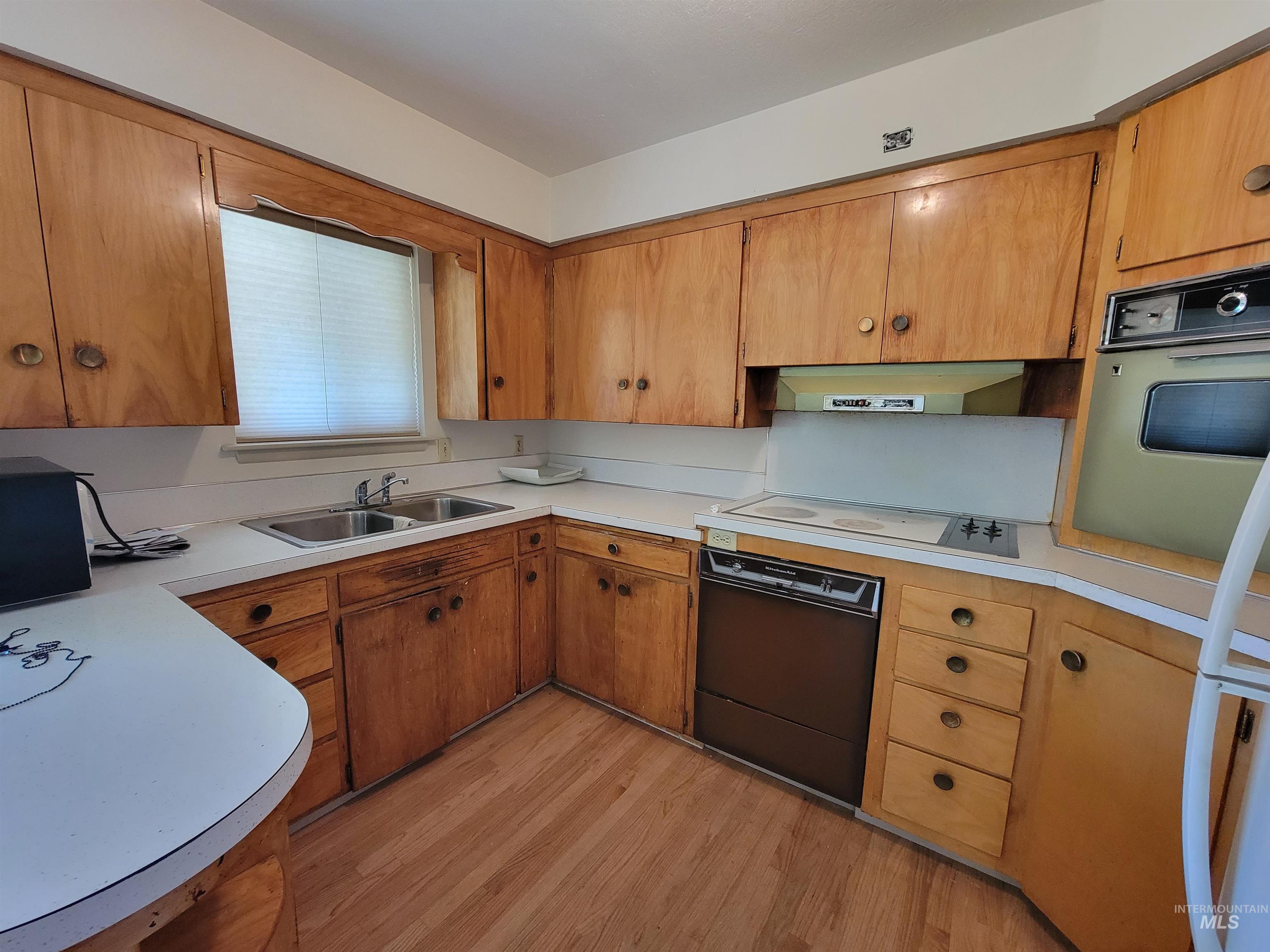 Kitchen with brown cabinetry, light countertops, light wood-type flooring, and dishwasher