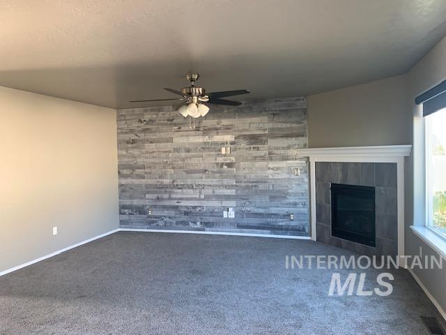 Unfurnished living room with a tile fireplace, ceiling fan, carpet flooring, and an accent wall