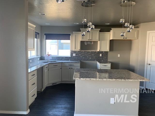 Kitchen featuring a center island, decorative light fixtures, light stone countertops, white cabinetry, and dark wood finished floors