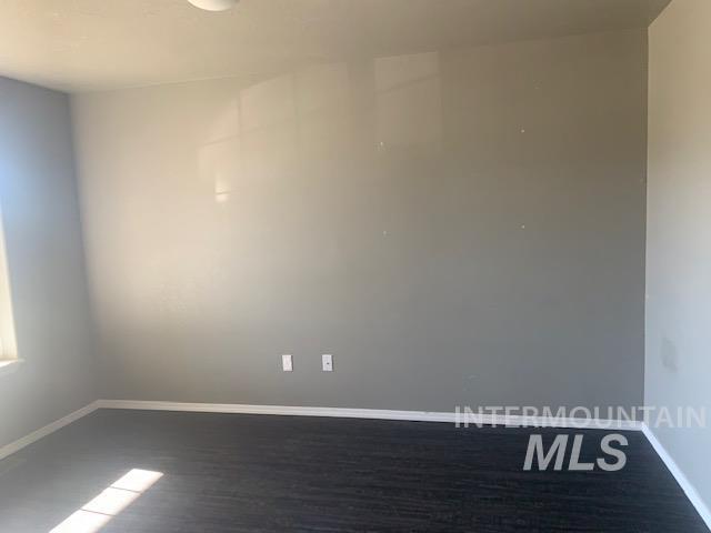 Unfurnished room featuring baseboards and dark wood-style flooring
