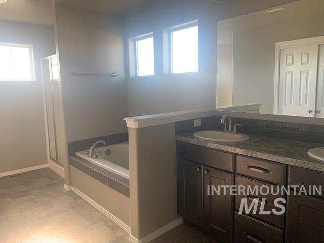 Bathroom featuring double vanity, a stall shower, a garden tub, and dark floors