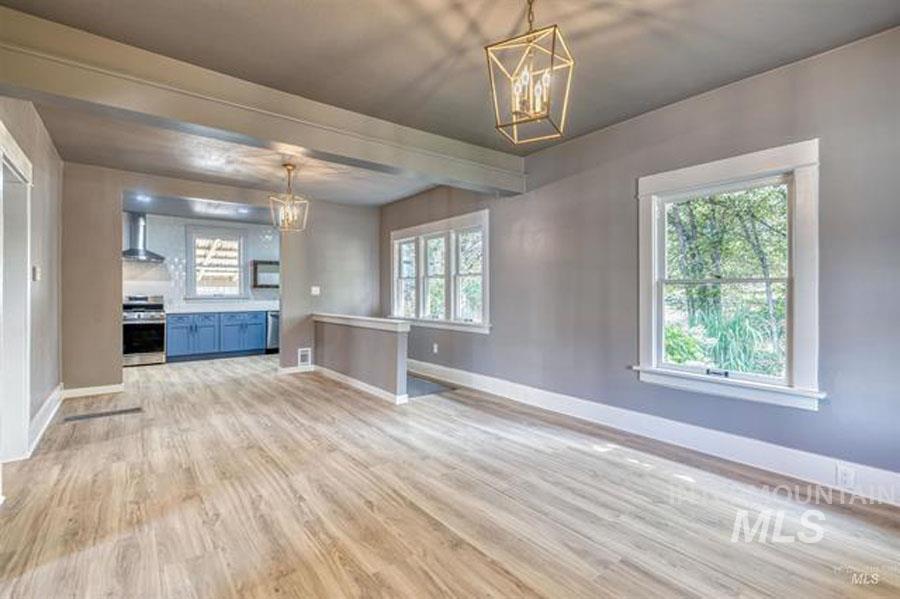 Unfurnished living room featuring light wood-type flooring, a chandelier, and beam ceiling