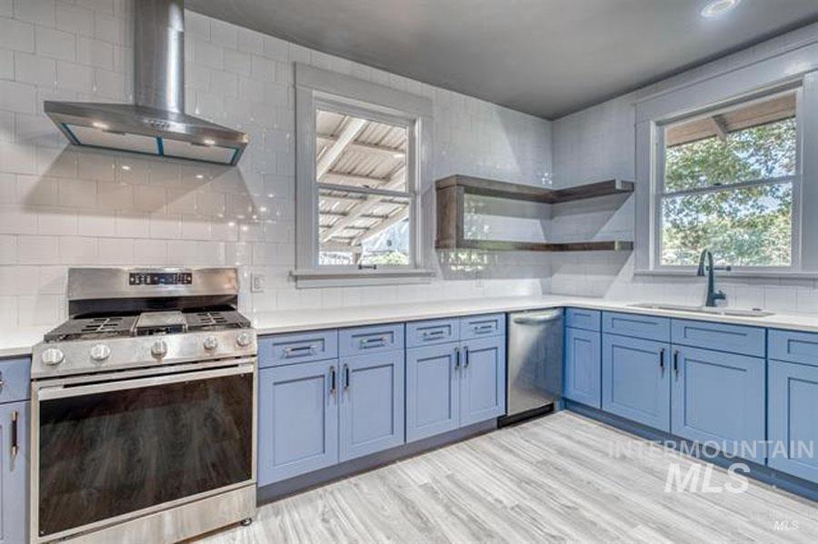 Kitchen featuring stainless steel appliances, wall chimney range hood, open shelves, and tasteful backsplash