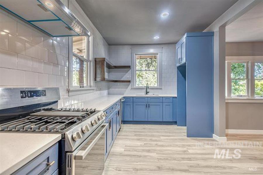 Kitchen with gas range, exhaust hood, backsplash, open shelves, and blue cabinets