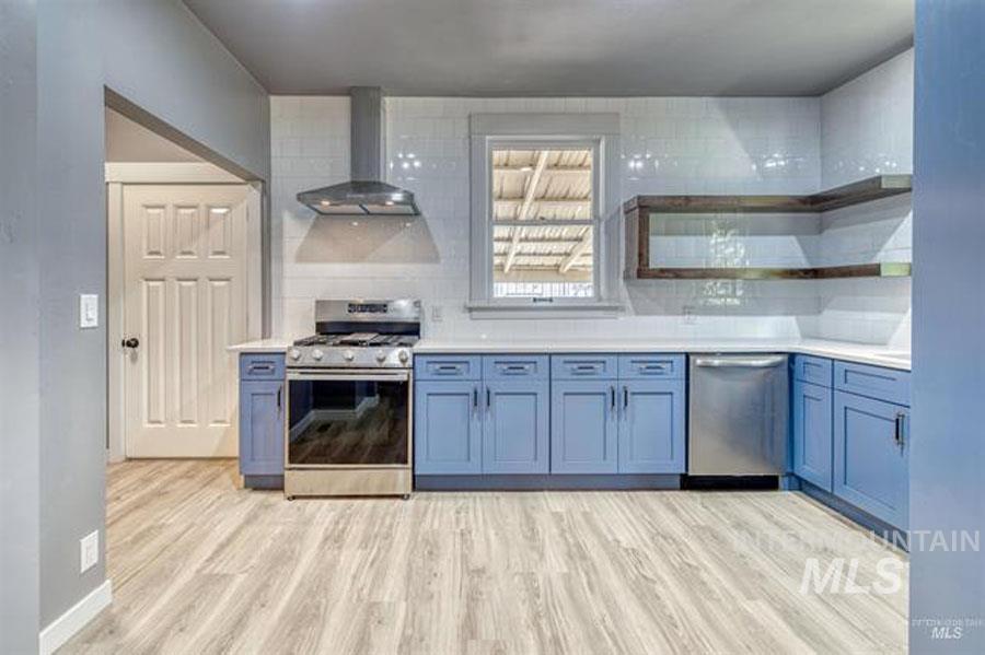 Kitchen with stainless steel appliances, wall chimney exhaust hood, backsplash, light wood-style floors, and open shelves