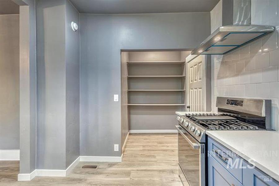 Kitchen featuring stainless steel range with gas cooktop, wall chimney exhaust hood, backsplash, light wood-style flooring, and light stone counters