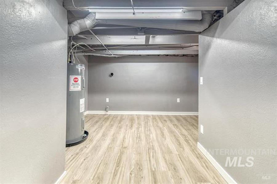 Basement with a textured wall, water heater, and light wood finished floors
