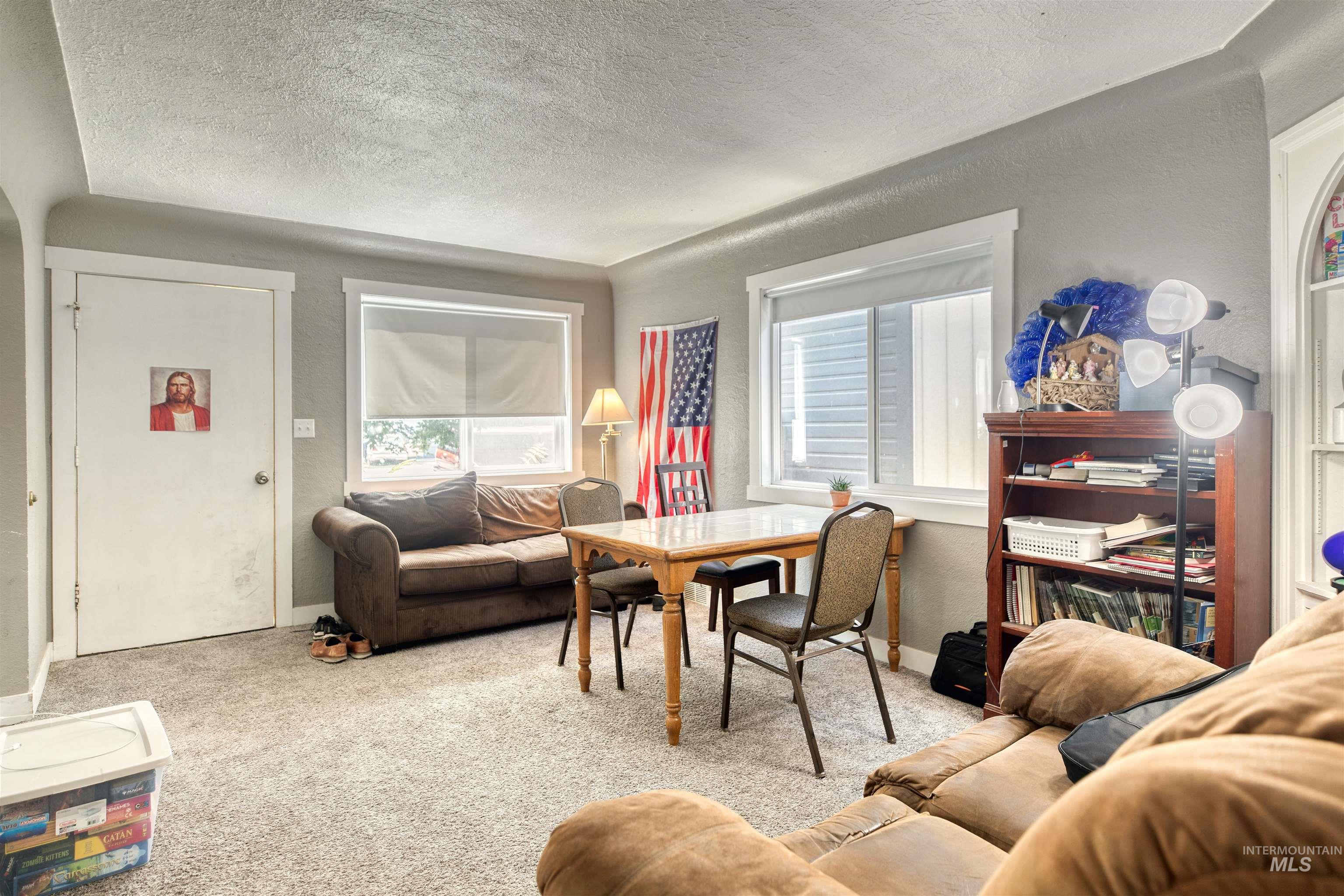 Living area with a textured wall, light colored carpet, and a textured ceiling