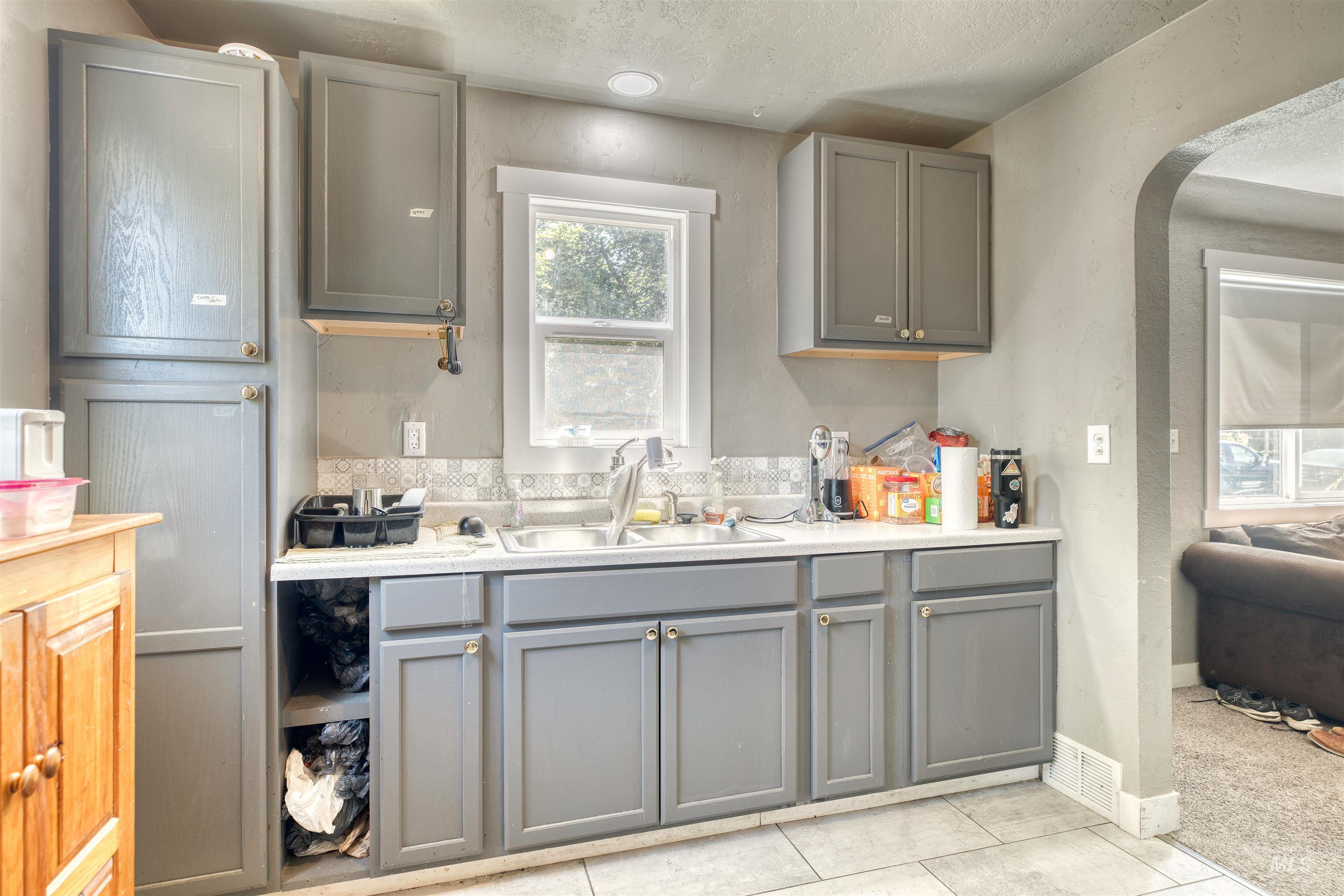 Kitchen with gray cabinets, light countertops, arched walkways, light tile patterned flooring, and a textured ceiling