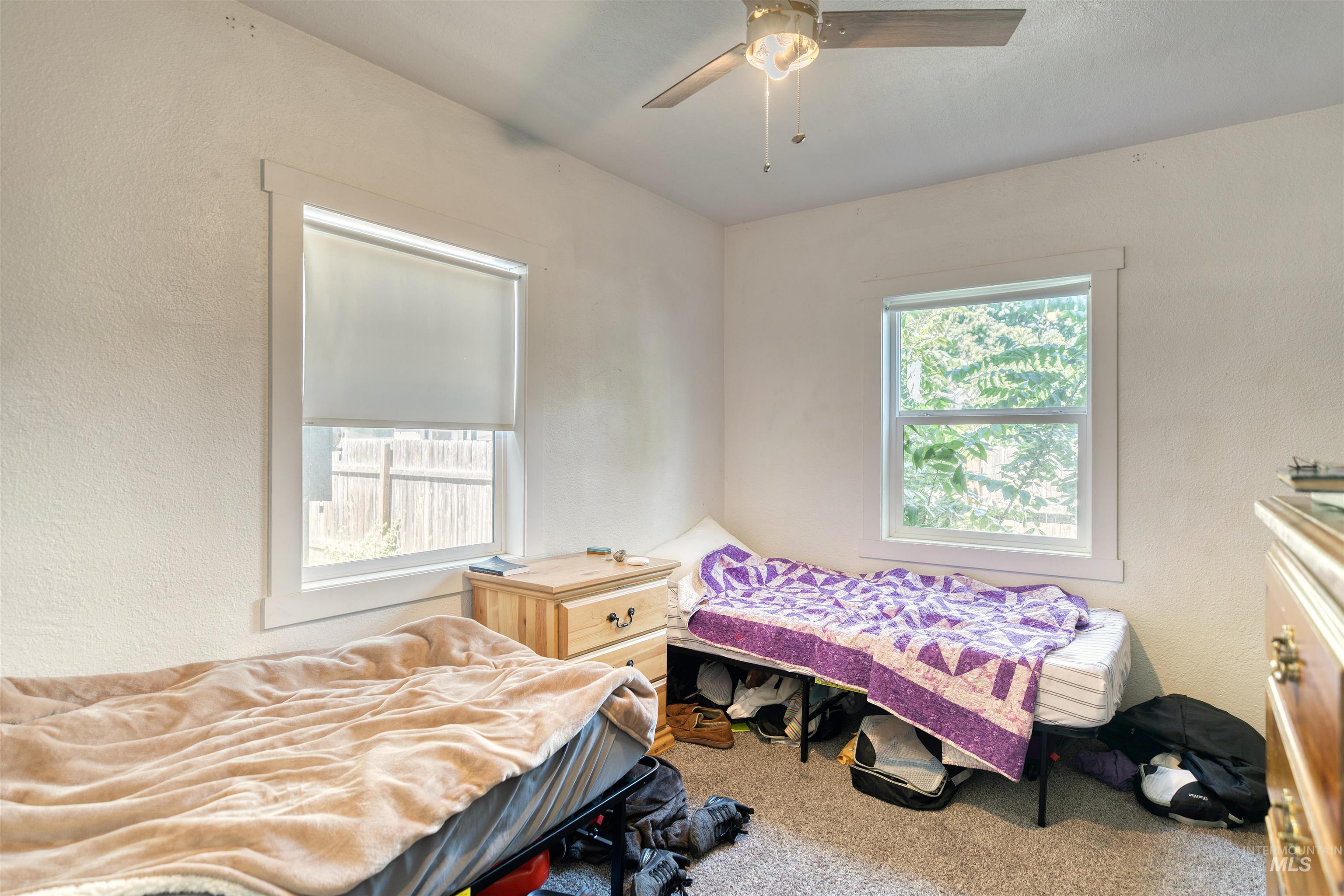 Bedroom featuring a textured wall, multiple windows, carpet floors, and a ceiling fan