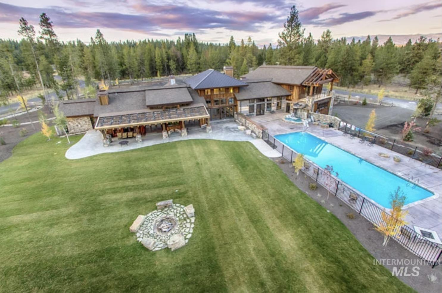 Back of house at dusk featuring a patio, stone siding, a community pool, a chimney, and a wooded view