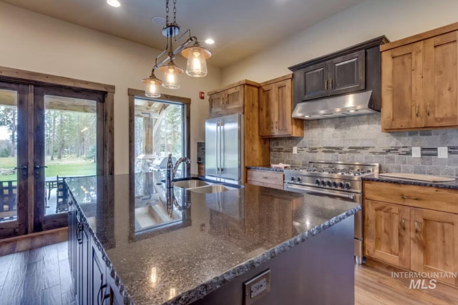 Kitchen with dark stone countertops, decorative light fixtures, wood finished floors, decorative backsplash, and an island with sink