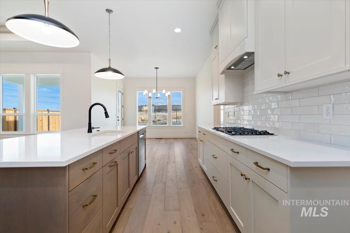 Kitchen with decorative light fixtures, a kitchen island with sink, light wood-type flooring, a chandelier, and white cabinetry