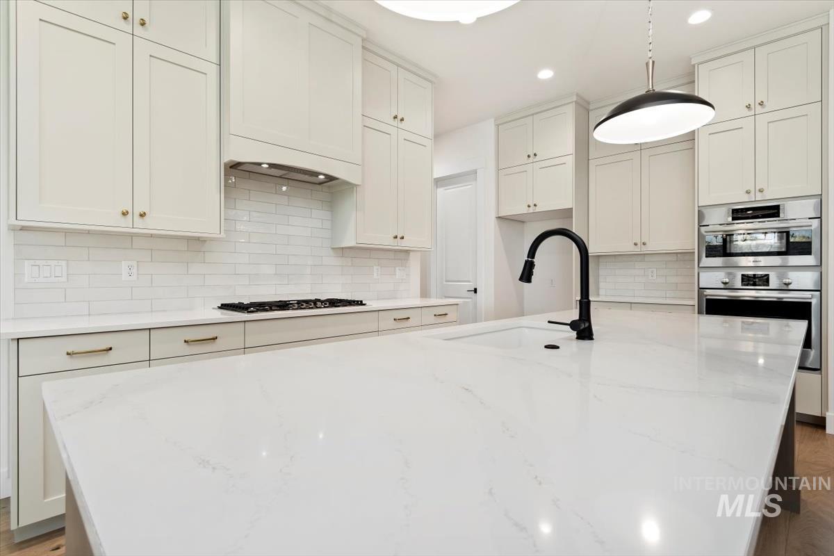 Kitchen featuring light stone counters, a center island with sink, white cabinetry, decorative backsplash, and recessed lighting