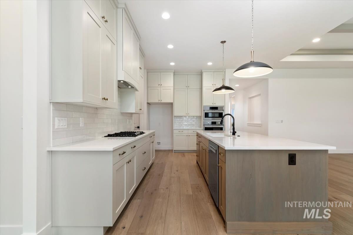 Kitchen with backsplash, a kitchen island with sink, light wood-type flooring, white cabinetry, and hanging light fixtures
