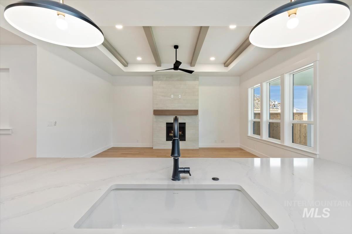 Kitchen view of beam ceiling, light stone countertops, a large fireplace, ceiling fan, and recessed lighting