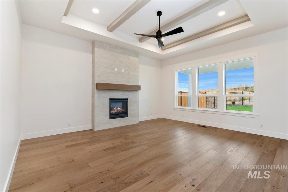 Unfurnished living room with light wood-style floors, a fireplace, a ceiling fan, recessed lighting, and a tray ceiling