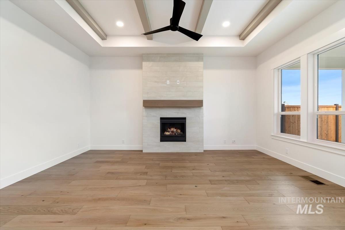 Unfurnished living room featuring a tile fireplace, light wood finished floors, ceiling fan, recessed lighting, and a raised ceiling