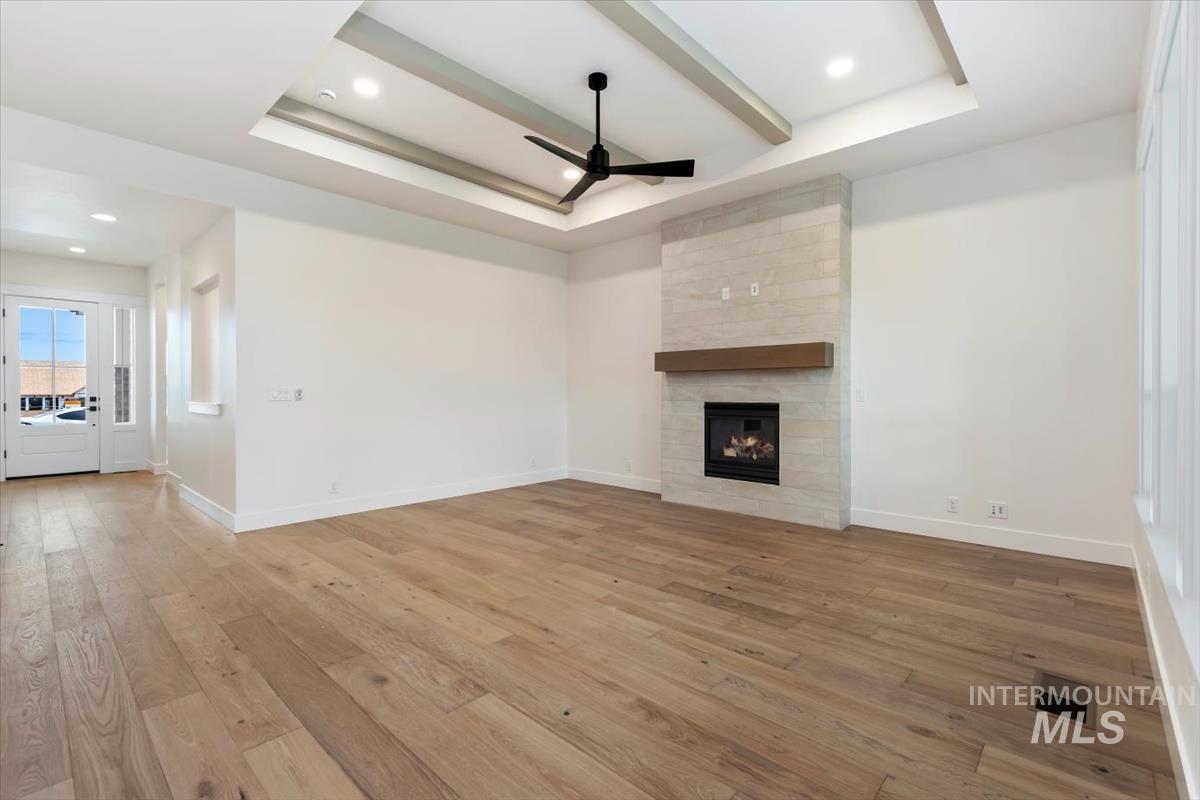 Unfurnished living room featuring a raised ceiling, light wood-style flooring, a ceiling fan, a fireplace, and recessed lighting
