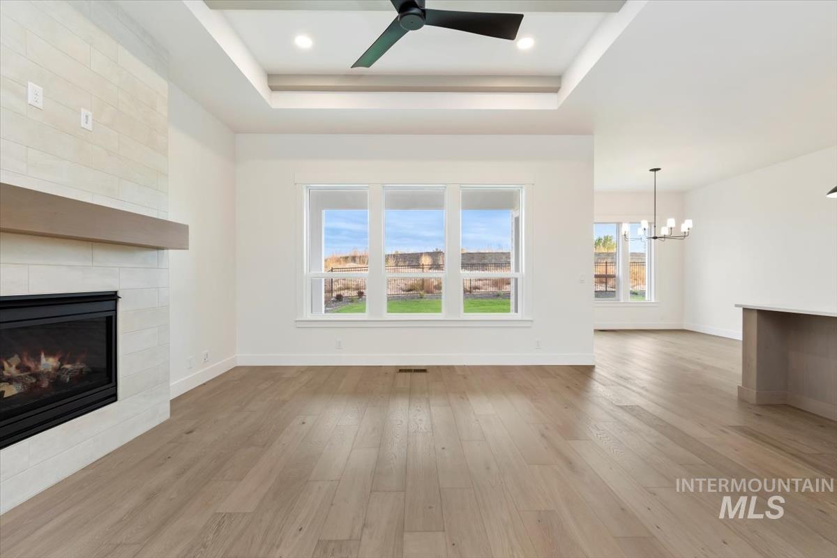 Unfurnished living room with light wood finished floors, ceiling fan, a fireplace, a raised ceiling, and a chandelier