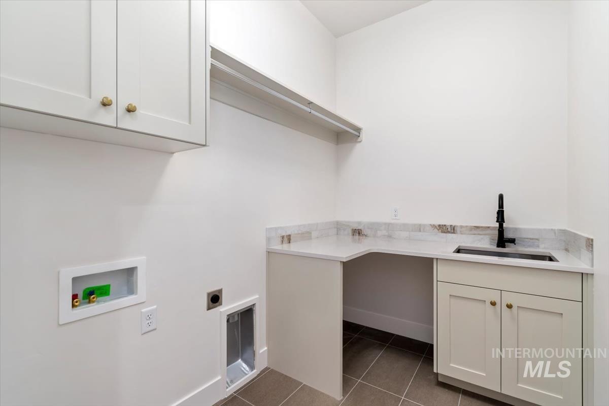 Laundry area with dark tile patterned floors, cabinet space, electric dryer hookup, and hookup for a washing machine