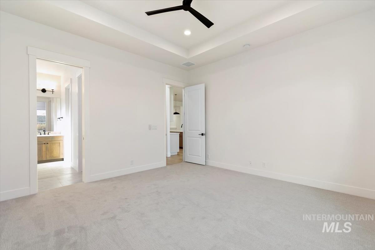 Unfurnished bedroom with a tray ceiling, light carpet, ceiling fan, recessed lighting, and ensuite bath
