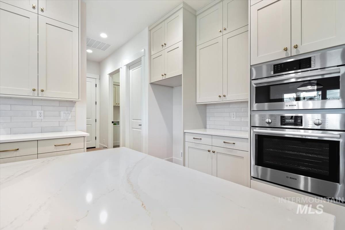 Kitchen with double oven, light stone counters, white cabinets, recessed lighting, and backsplash