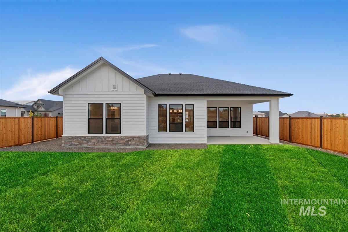 Rear view of house with a patio area, stone siding, a fenced backyard, roof with shingles, and board and batten siding