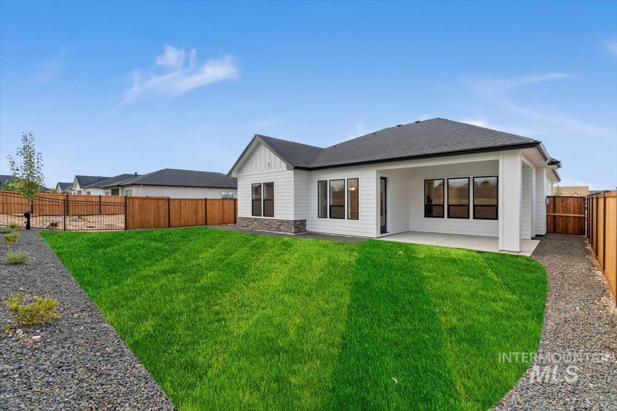 Rear view of property with stone siding, a patio area, a fenced backyard, roof with shingles, and board and batten siding