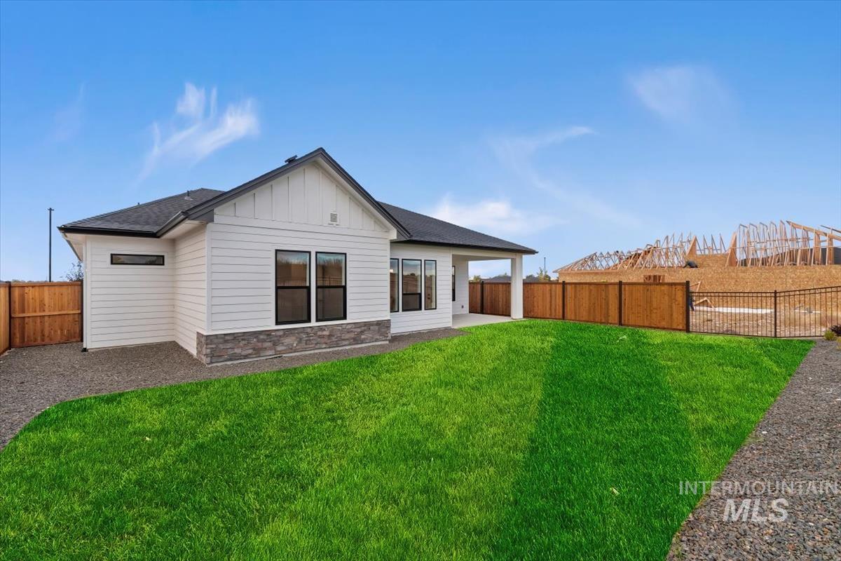 Rear view of property with stone siding, a patio area, board and batten siding, a fenced backyard, and a shingled roof