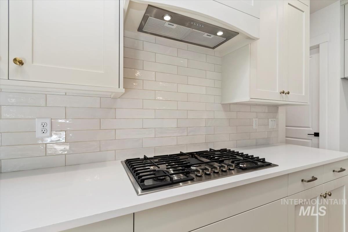 Kitchen featuring white cabinets, exhaust hood, stainless steel gas stovetop, decorative backsplash, and light stone countertops