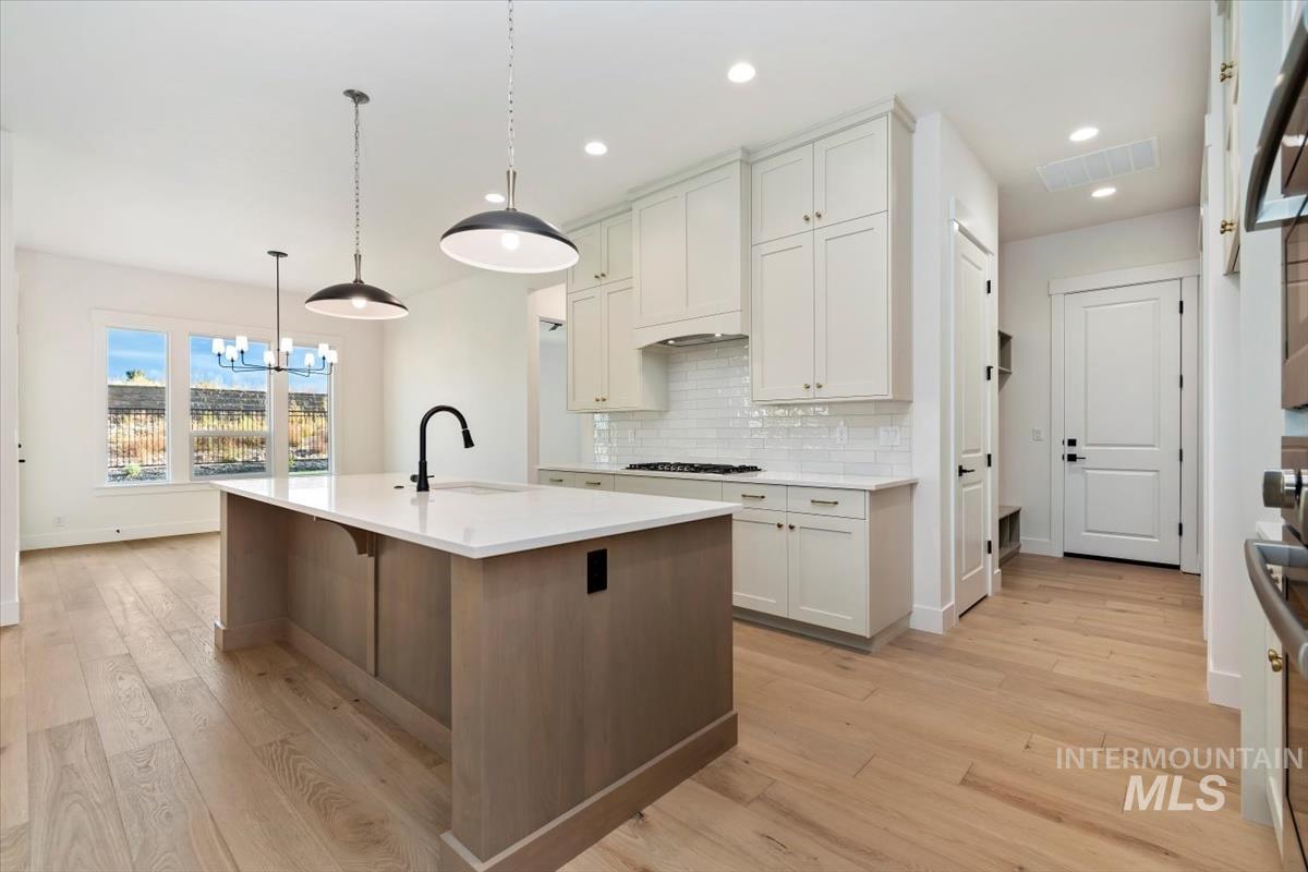 Kitchen with backsplash, white cabinetry, a chandelier, decorative light fixtures, and a kitchen island with sink