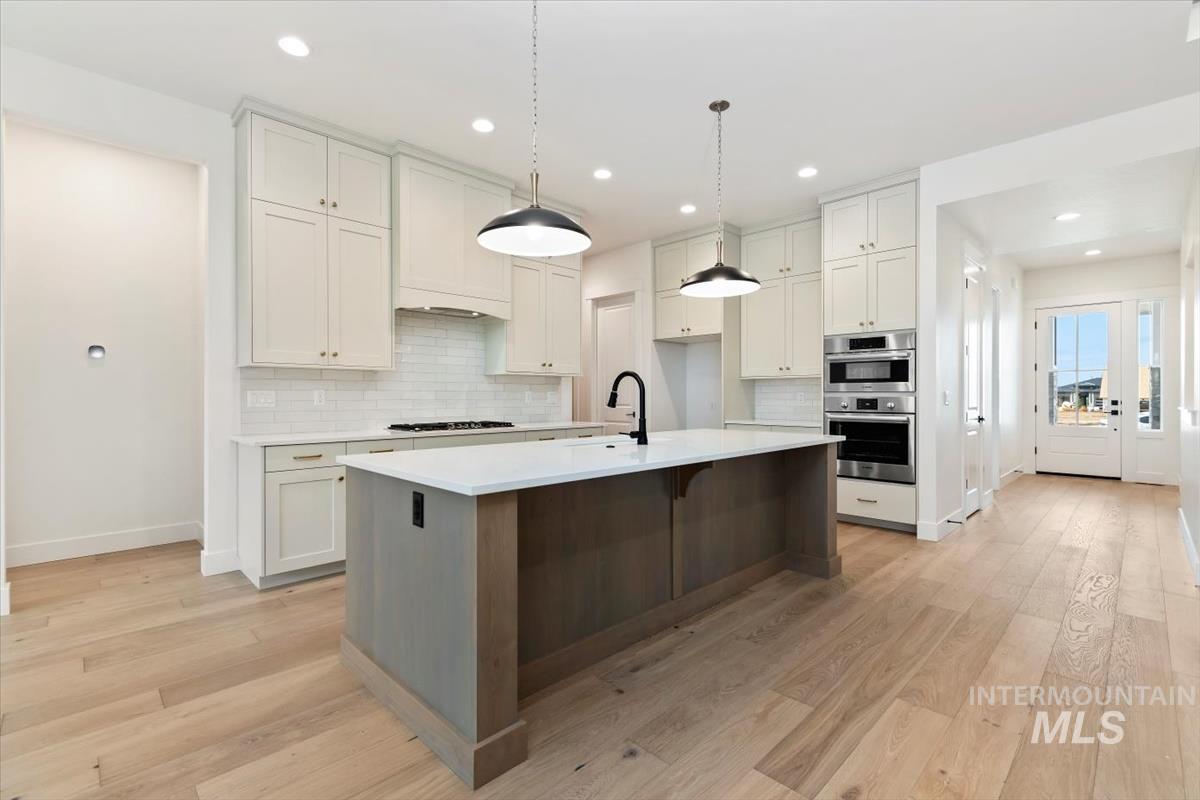 Kitchen with an island with sink, white cabinets, decorative light fixtures, a kitchen breakfast bar, and recessed lighting