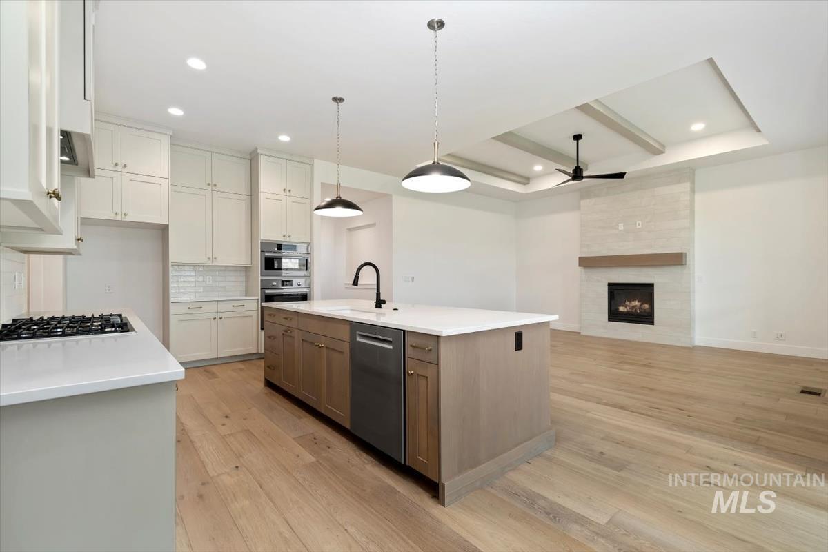 Kitchen featuring beam ceiling, ceiling fan, tasteful backsplash, light wood finished floors, and decorative light fixtures