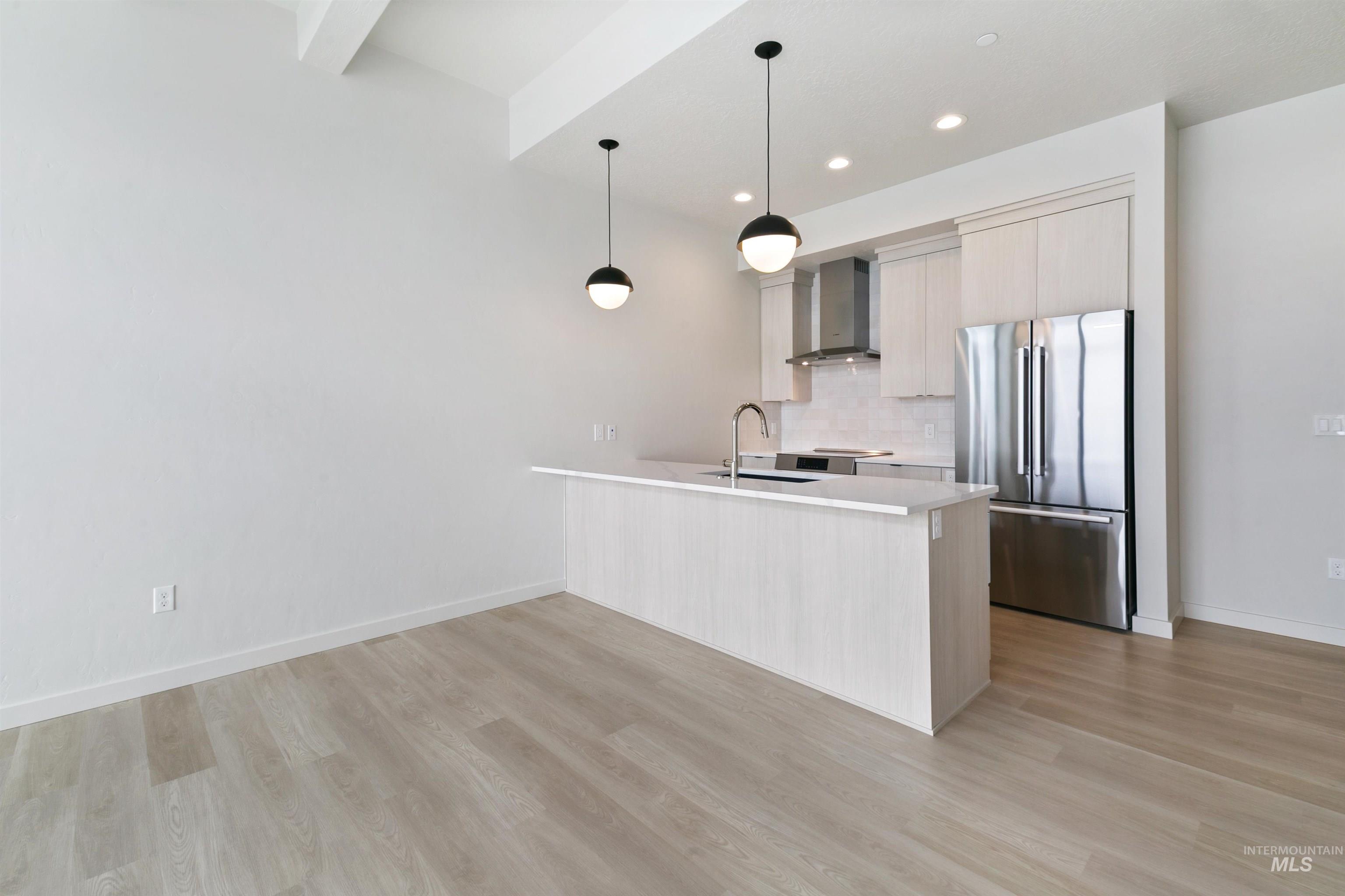Kitchen featuring freestanding refrigerator, modern cabinets, a peninsula, pendant lighting, and wall chimney range hood