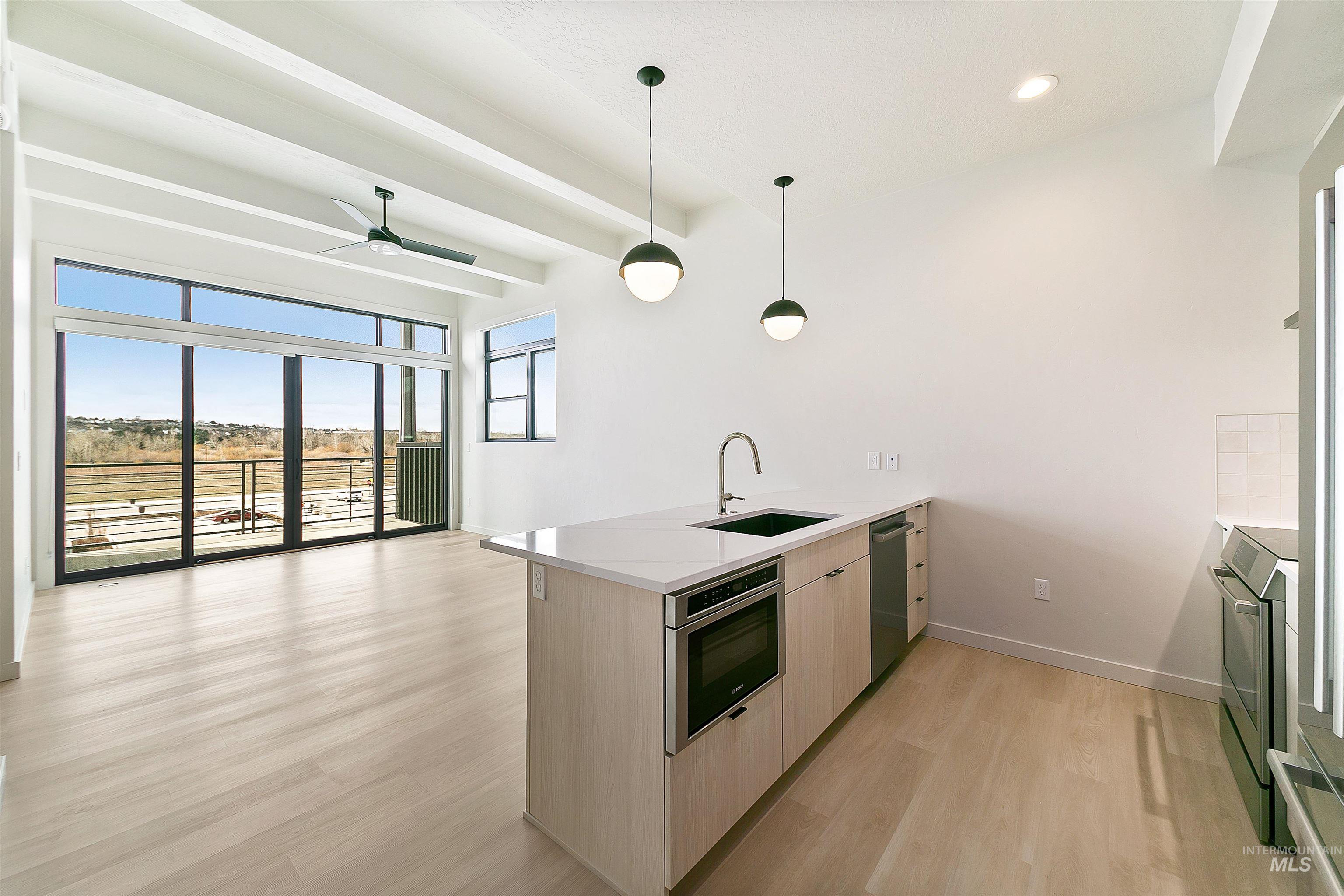 Kitchen with a peninsula, light wood-type flooring, open floor plan, pendant lighting, and light brown cabinets