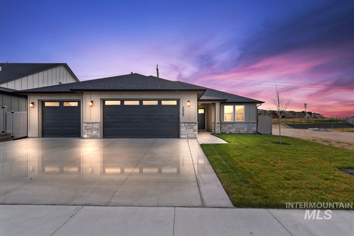 View of front of home with stone siding, a shingled roof, a garage, and driveway