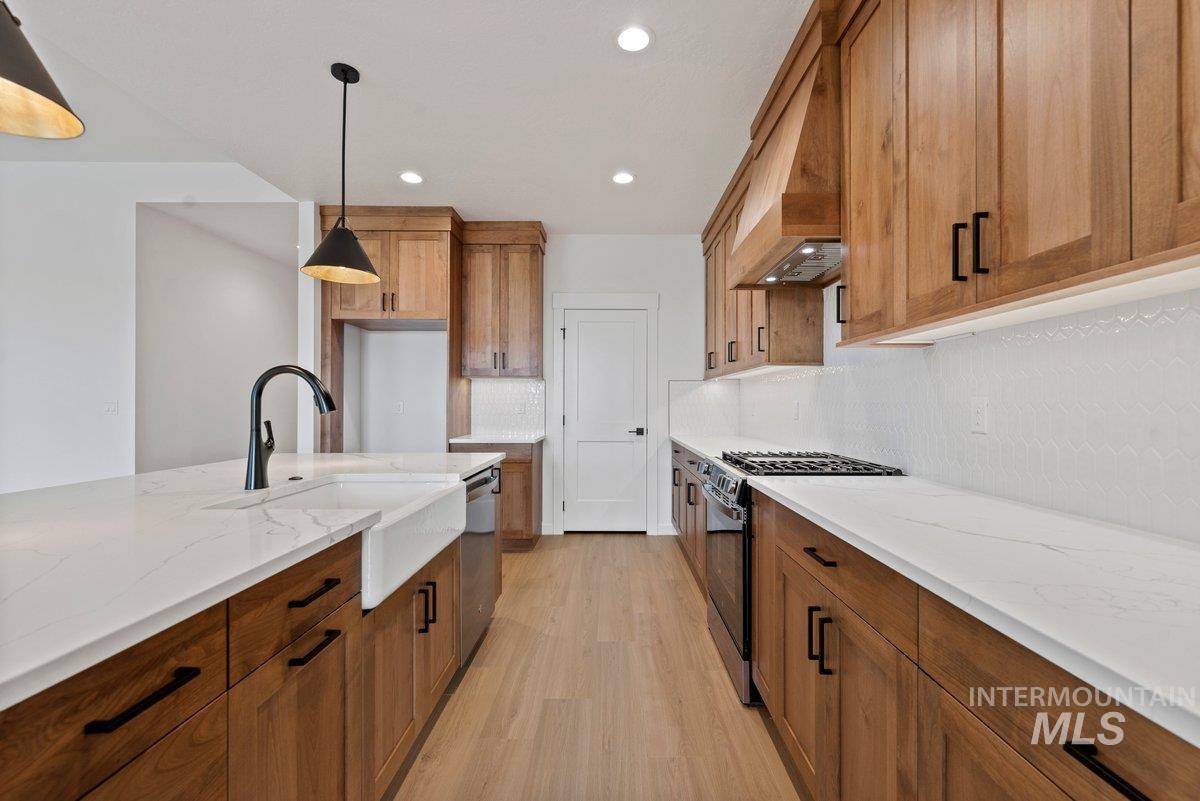 Kitchen featuring brown cabinets, appliances with stainless steel finishes, light stone counters, decorative light fixtures, and light wood finished floors