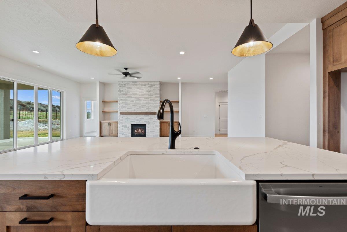 Kitchen featuring dishwasher, light stone countertops, a fireplace, brown cabinetry, and open floor plan