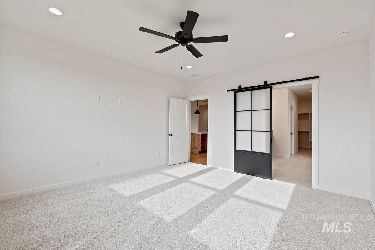 Unfurnished bedroom with a barn door, light carpet, a ceiling fan, and recessed lighting
