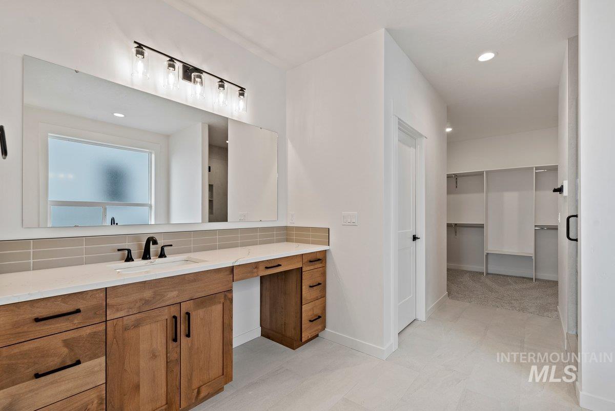 Bathroom featuring vanity, a walk in closet, backsplash, and recessed lighting
