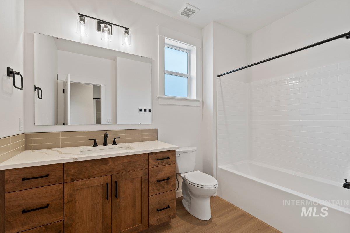 Full bath featuring vanity, washtub / shower combination, tasteful backsplash, and light wood-style floors