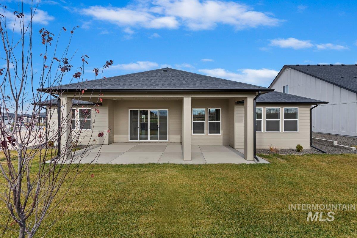 Back of house featuring a shingled roof, a patio area, and a lawn