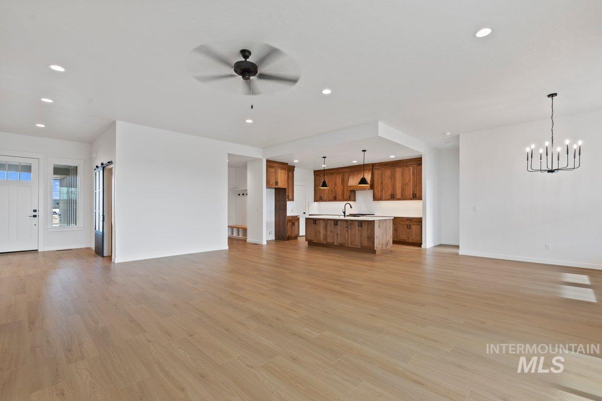 Unfurnished living room featuring recessed lighting, light wood-style floors, ceiling fan, and a chandelier