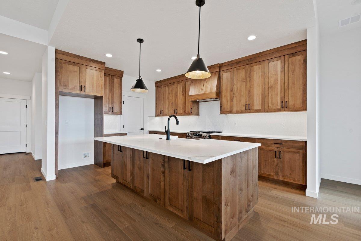Kitchen with brown cabinets, pendant lighting, a center island with sink, dark wood finished floors, and a kitchen breakfast bar