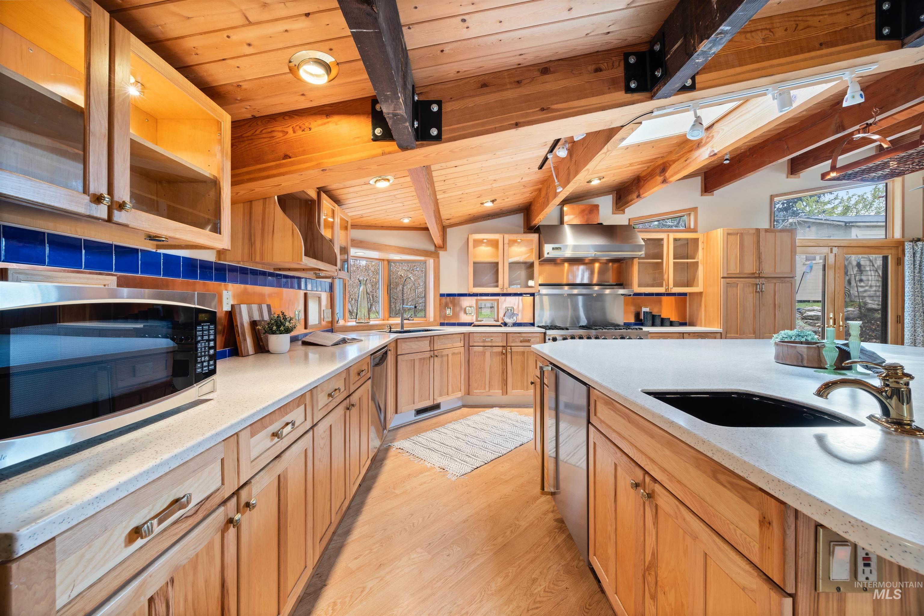 Kitchen with glass insert cabinets, stainless steel appliances, light wood-type flooring, light stone countertops, and wooden ceiling