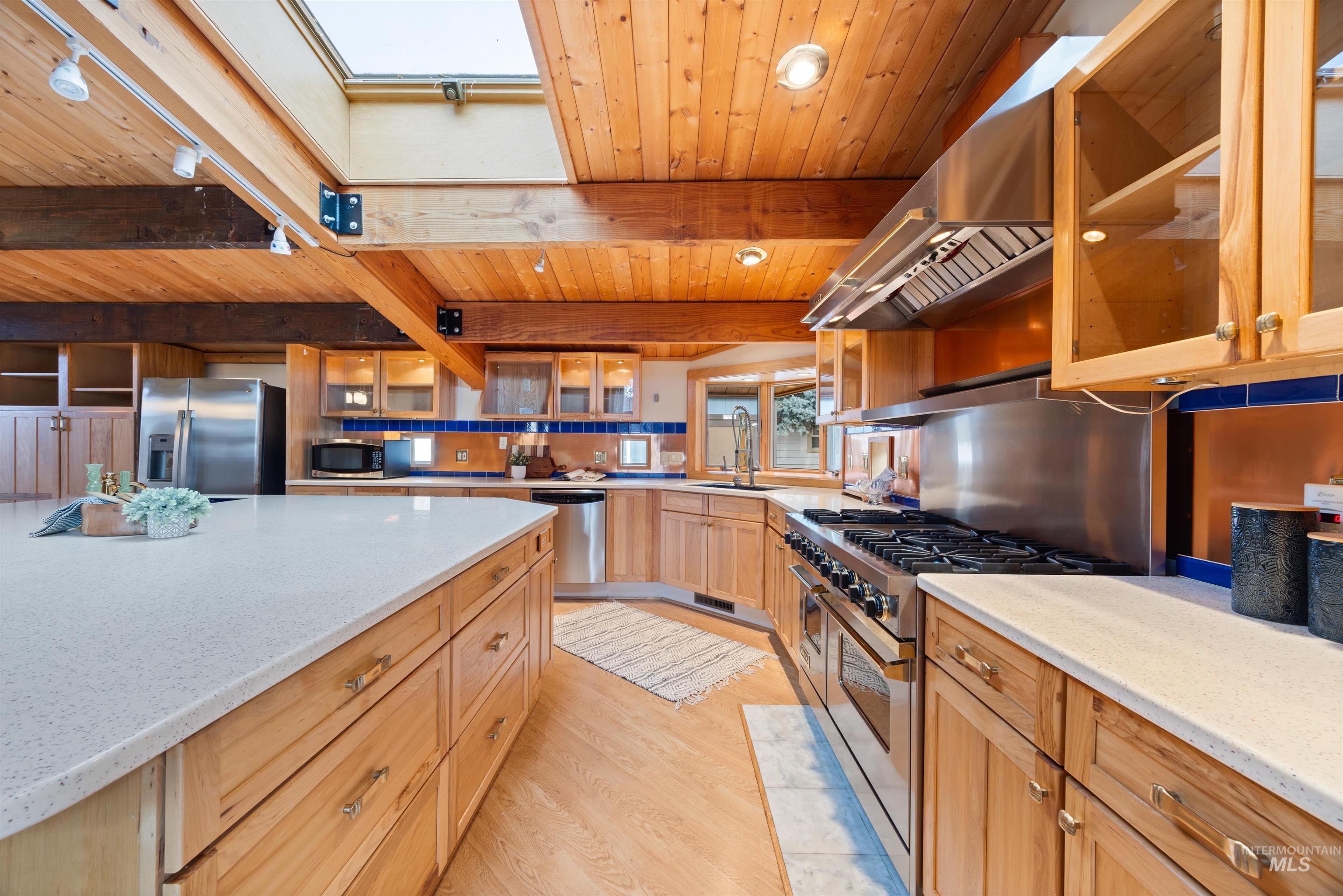 Kitchen with glass insert cabinets, a wooden ceiling with exposed beams, extractor fan, stainless steel appliances, and light stone countertops