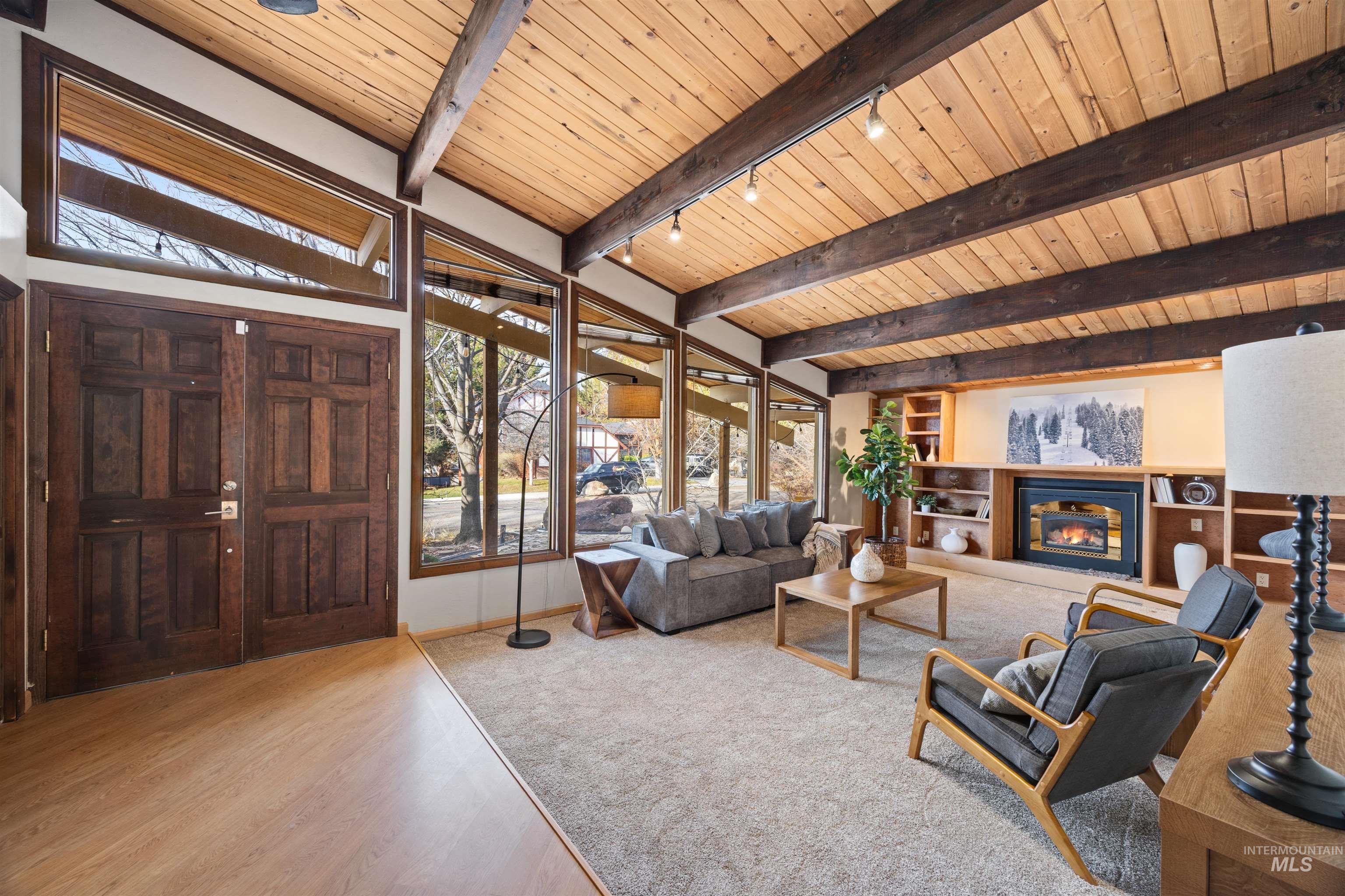 Living area with a glass covered fireplace, a wood ceiling with exposed beams, light wood-style floors, and track lighting