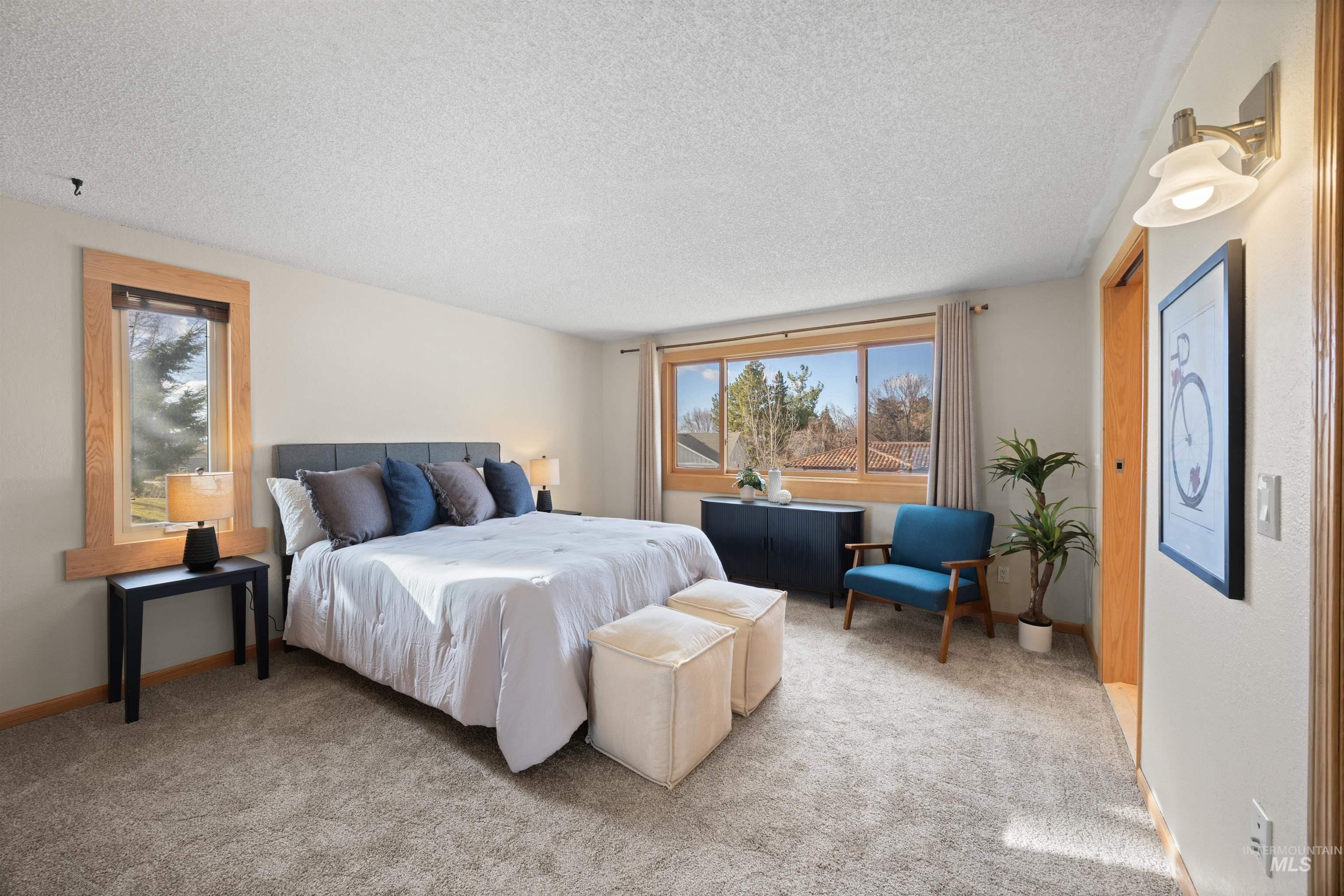 Carpeted bedroom with a textured ceiling and multiple windows