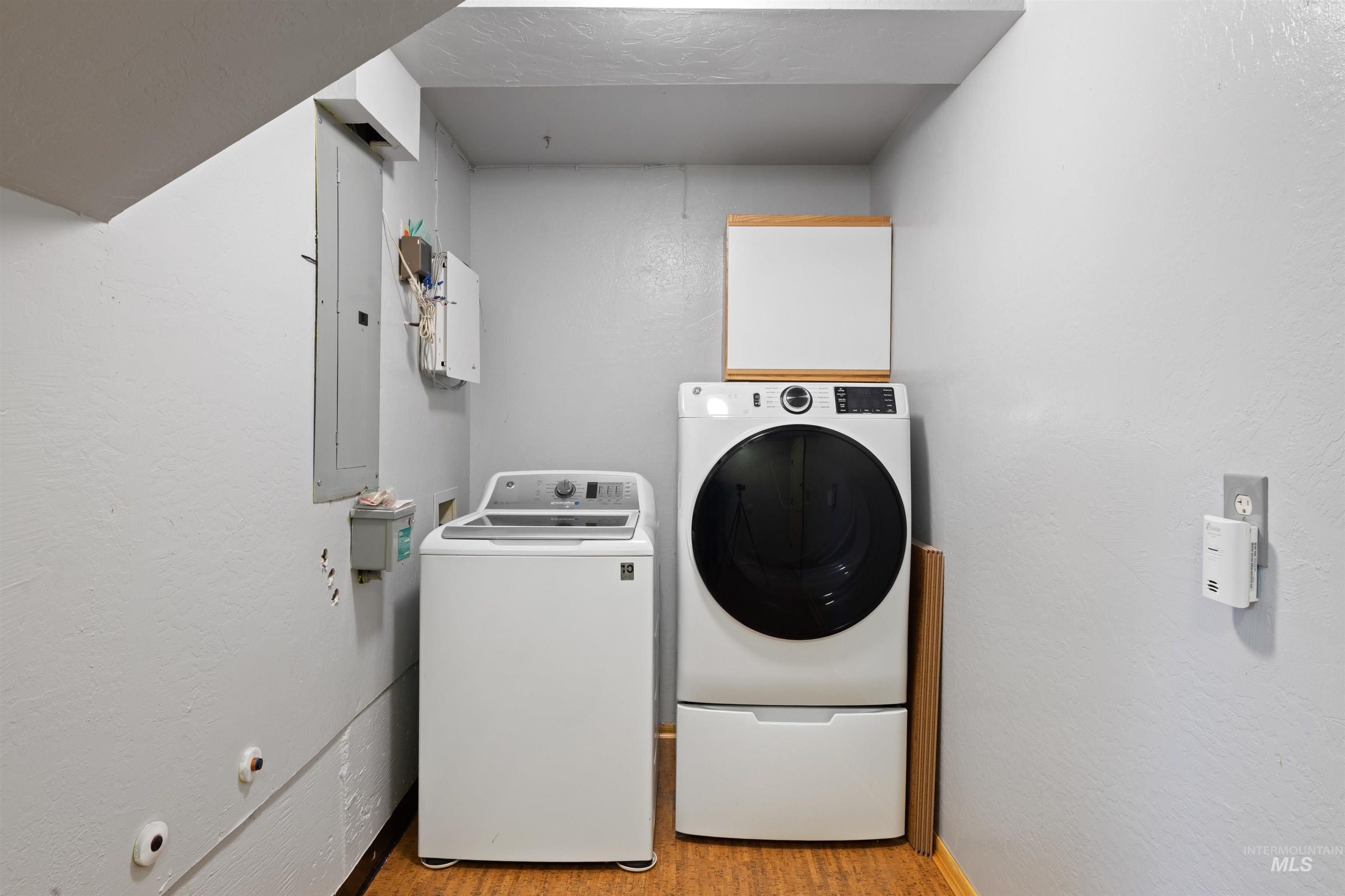Laundry area featuring washing machine and clothes dryer, a textured wall, electric panel, and light wood-style floors